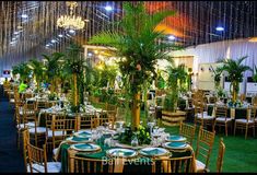 tables set up for an event with palm trees and greenery in the center, hanging from the ceiling