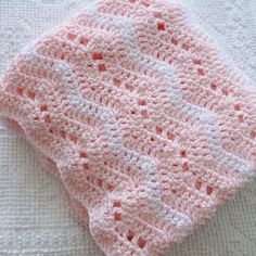 a pink and white knitted blanket laying on top of a bed