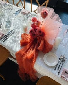 the table is set with silverware and pink flowers in an orange organe bag