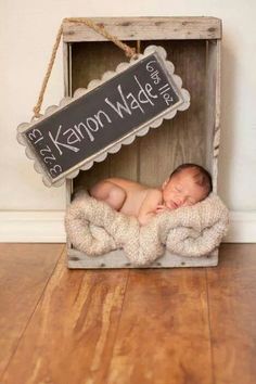 a baby is sleeping in a wooden crate with a chalkboard sign hanging from it's side