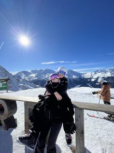 a woman sitting on top of a snow covered ski slope next to a wooden fence