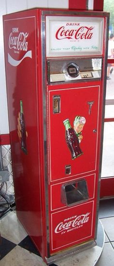 an old coca - cola machine sitting in front of a window