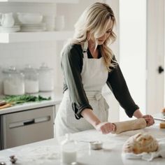 a woman in an apron rolling dough on a counter