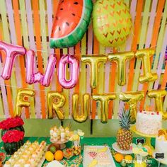 a table topped with lots of desserts and balloon letters that spell out the word fruit