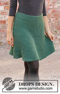 a woman standing in front of a brick wall wearing a green skirt and black tights