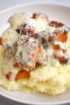 a white plate topped with mashed potatoes covered in gravy and parmesan cheese