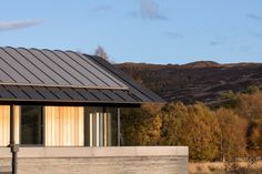 a small house with a metal roof in front of some hills and trees on the other side