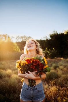 a woman holding flowers in her hands and smiling at the camera while standing in a field