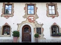 a white building with three windows and two potted plants on the outside wall,