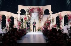 a man standing at the end of a stage with flowers and greenery on it