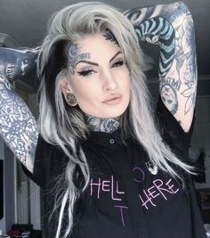 a woman with grey hair and tattoos on her arms, wearing a black shirt that says hell is here