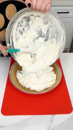 someone is mixing cream in a bowl on a red place mat with a spatula