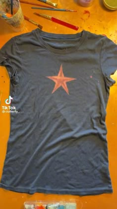 a t - shirt with a star painted on it sitting next to paintbrushes