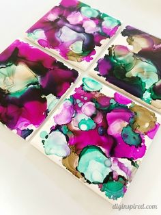 four square paintings with purple and green paint on them sitting on a white counter top