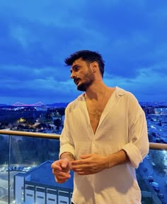 a man standing on top of a balcony next to a cityscape at night