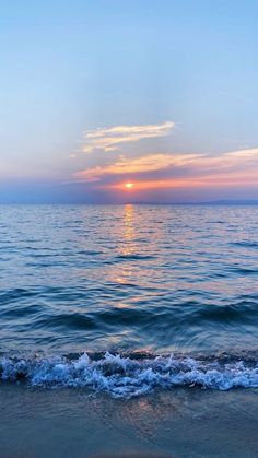 the sun is setting over the ocean with waves coming in to shore and blue sky