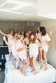 a group of women standing on top of a bed in pink robes posing for the camera