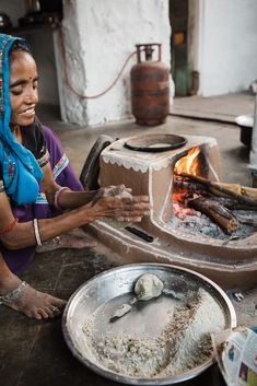 a woman is making something out of clay with a fire in the oven behind her