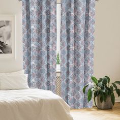 a white bed sitting next to a window covered in blue and pink curtains on top of a wooden floor