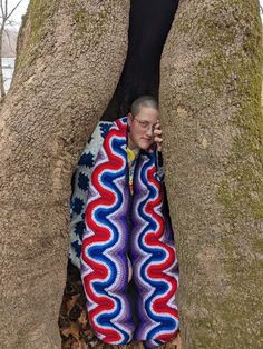 a young boy is wrapped up in a blanket while talking on his cell phone next to a large tree