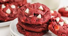 red velvet cookies with white chocolate chips are stacked on top of each other in front of a glass of milk