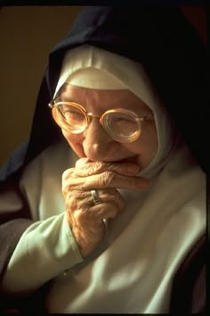 an older woman wearing glasses and a nun outfit with her hands on her chin, looking at the camera