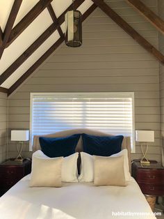 a bed with white sheets and blue pillows in a room that has wooden beams on the ceiling