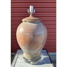 a large vase sitting on top of a table next to a red wall in front of a building