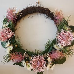 a wreath with pink flowers and greenery hanging on the wall next to a white wall