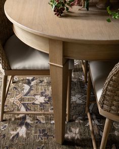 a wooden table with two chairs and a vase on it's end, in front of a patterned area rug