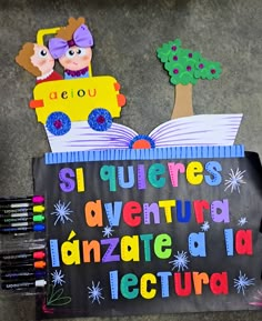 a bulletin board with an open book and some crayons next to it on the ground