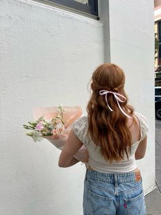 a woman with red hair holding a bouquet of flowers in her left hand and looking out the window