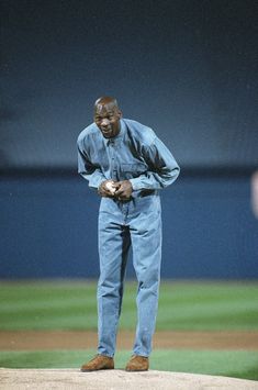 a man standing on top of a baseball field with his hands in his pockets while holding a ball