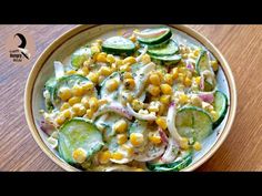 a bowl filled with cucumber, corn and cheese salad on top of a wooden table