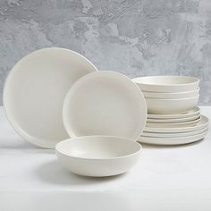 a stack of white dishes sitting on top of a table next to each other in front of a gray wall