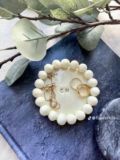 two white beaded bracelets sitting on top of a blue tray next to a plant