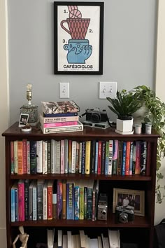 a bookshelf filled with lots of books next to a plant and pictures on the wall