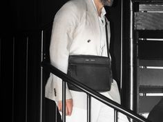 a man wearing a white suit carrying a black bag while walking down a stair case