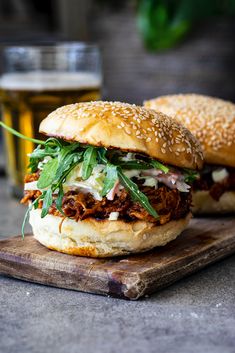 two pulled pork sandwiches on a cutting board next to a glass of beer