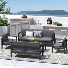 an outdoor living area with grey couches and chairs next to a bar overlooking the ocean