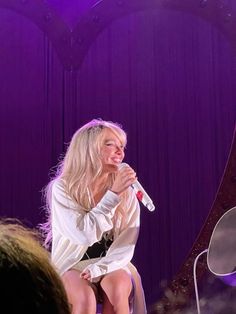 a woman sitting on top of a chair while holding a microphone in her right hand