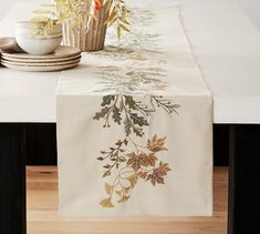 the table is set with plates and cups on it, along with an embroidered leaf runner