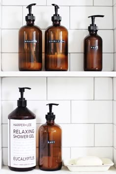 three brown bottles are sitting on the shelf in front of white tiles and soap dispensers