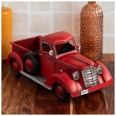 a red toy truck sitting on top of a wooden table next to a brown vase