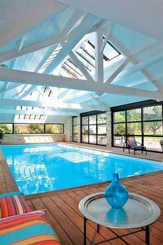 an indoor swimming pool surrounded by windows and wood flooring, with chairs around it