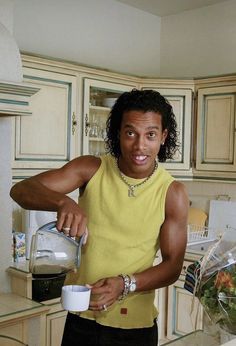 a man in a yellow shirt is pouring something into a white cup and smiling at the camera