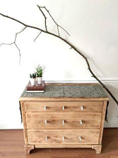 a wooden dresser sitting on top of a hard wood floor next to a tree branch