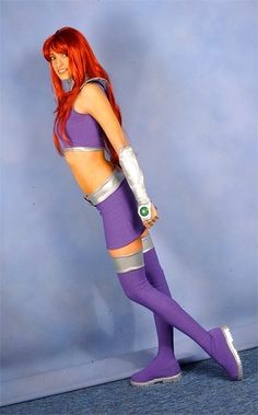 a woman with red hair and purple outfit posing for a photo in front of a blue wall