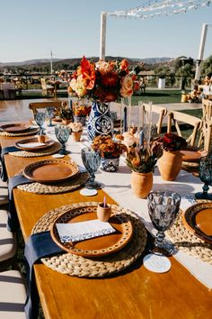 an outdoor table set with place settings and flowers in vases on the table top