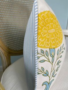 a close up of a chair with a pillow on it's back and a yellow flower in the center